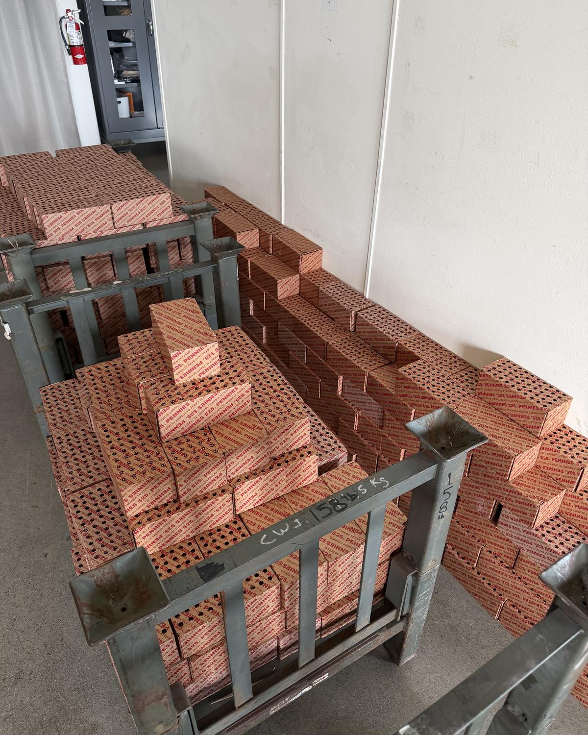 Stacks of red and white boxes printed PENNIES, loaded on grey steel racks in a storage room.